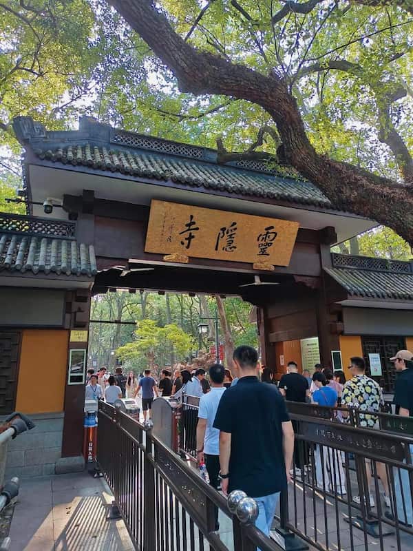 The grand main gate of Lingyin Temple in Hangzhou, with traditional Chinese architecture, red walls, and a golden plaque inscribed with the temple’s name.