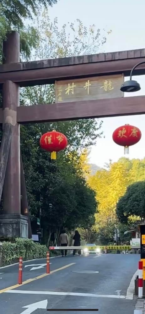 The traditional entrance gate of Longjing Village (Dragon Well Village) in Hangzhou, surrounded by lush tea plantations and rolling hills.