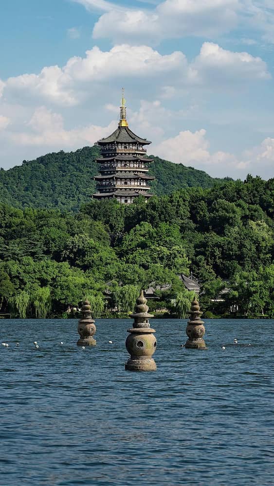 Scenic view of Hangzhou West Lake at sunset, with traditional boats and willow trees reflecting on the water.