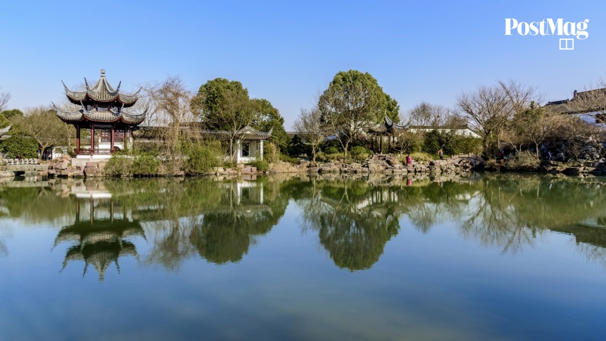 A long straight boardwalk stretching between two stretches of water with golden reed beds on both sides at Xixi Wetland
